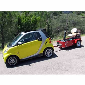 A small electric car pulling a mobility scooter on a ScootaTrailer